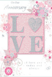 In this softly romantic anniversary card, the design unfolds like a delicate bouquet painted across a blush pink sky, creating a tranquil mood that suits intimate celebrations at home in Barking. The central feature is the word LOVE, prominently displayed in raised lettering that glitters subtly in the light. Each letter is filled with a gentle pearly tone, edged with fine silver sparkle that suggests a dusting of frost, offering both visual interest and an inviting, tactile sensation. Surrounding this word is a halo of stylised flowers and sweeping foliage, drawn with the same care a florist might take when planning a bespoke anniversary arrangement. The blossoms, shaded in blush, white, and hints of light grey, are outlined with delicate lines and occasional silver accents that shimmer like sunlight on the River Roding. Slim, curving stems and tendrils loop and spiral around the flowers, giving the whole card a sense of movement, as if a soft breeze is drifting across a garden. The background is a smooth, even pink, slightly muted to keep the mood gentle and refined, allowing the floral detailing and raised lettering to take centre stage. Tucked tastefully within the design is an anniversary message in graceful script, expressing heartfelt love and appreciation without overpowering the artwork. This card feels like a paper echo of a fresh bouquet delivered in Barking-from homes near Barking Abbey ruins to new apartments around the town centre-making it a tender keepsake to accompany real flowers and mark another year of shared memories.